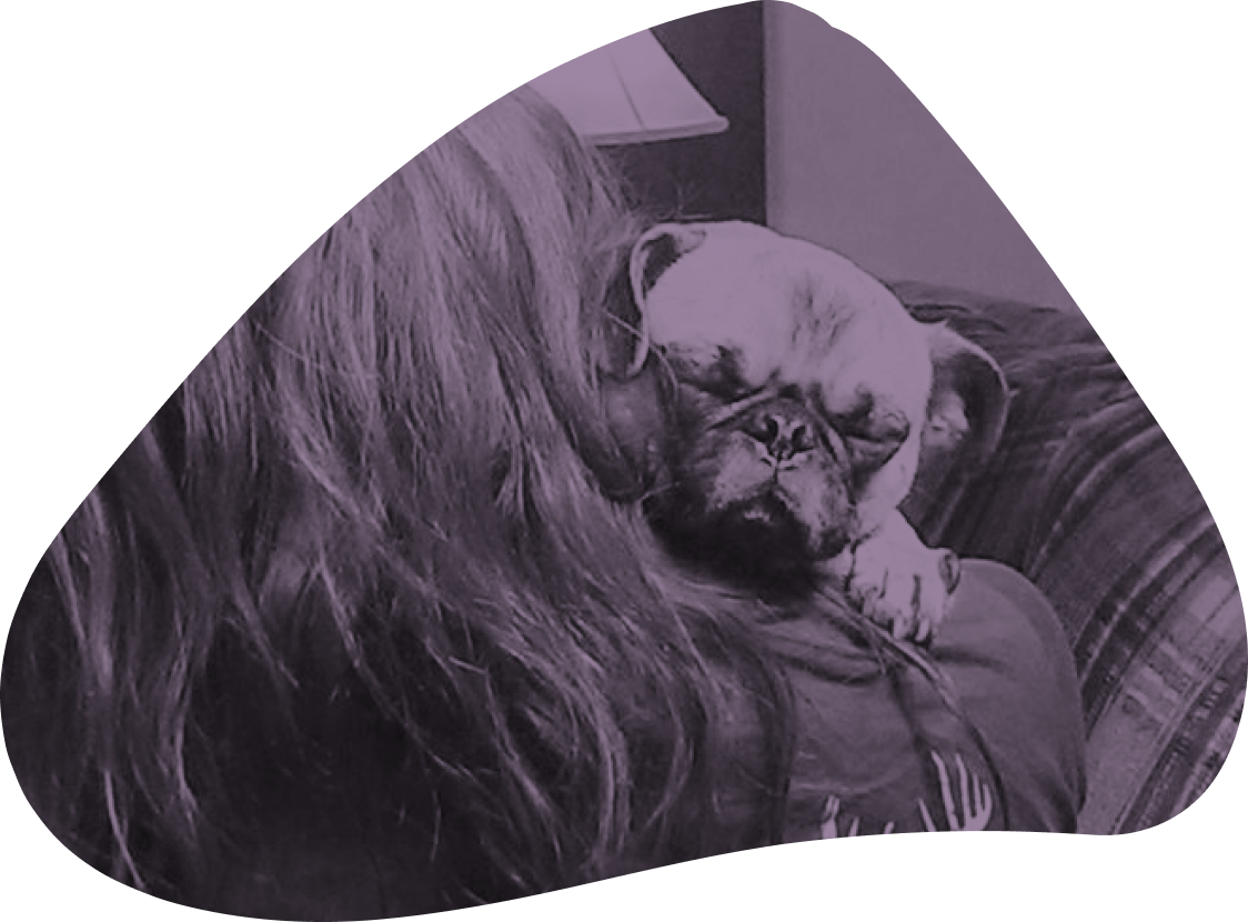 Person with long hair cuddling two small dogs, one white and one dark-colored, on a couch.